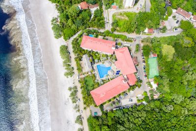 Aerial view of a beachfront resort with red roofs, pool, and surrounding tropical greenery in Playa Flamingo, Costa Rica