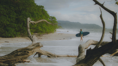 Surfer walking on Tamarindo Costa Rica beach with waves and lush forest