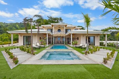 Front exterior of Casa Camari Potrero with twin pools, landscaped lawn, and covered terraces in La Marcela