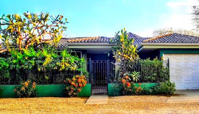Front exterior of Casa Motmot Playa Potrero with gated entry, garage, and lush tropical plants.