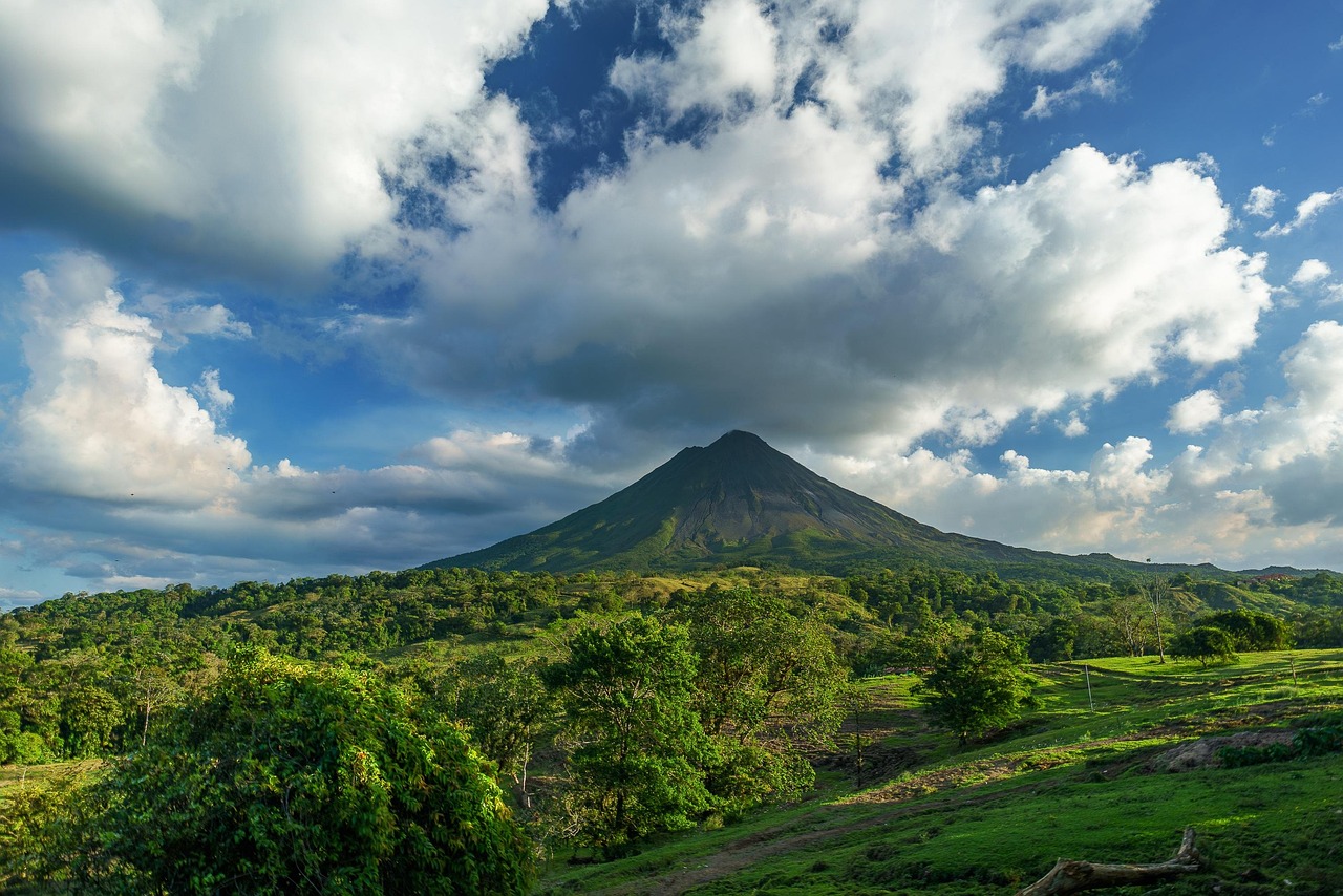 Arenal Volcano rising above lush green hills and forests under a partly cloudy Costa Rica sky.