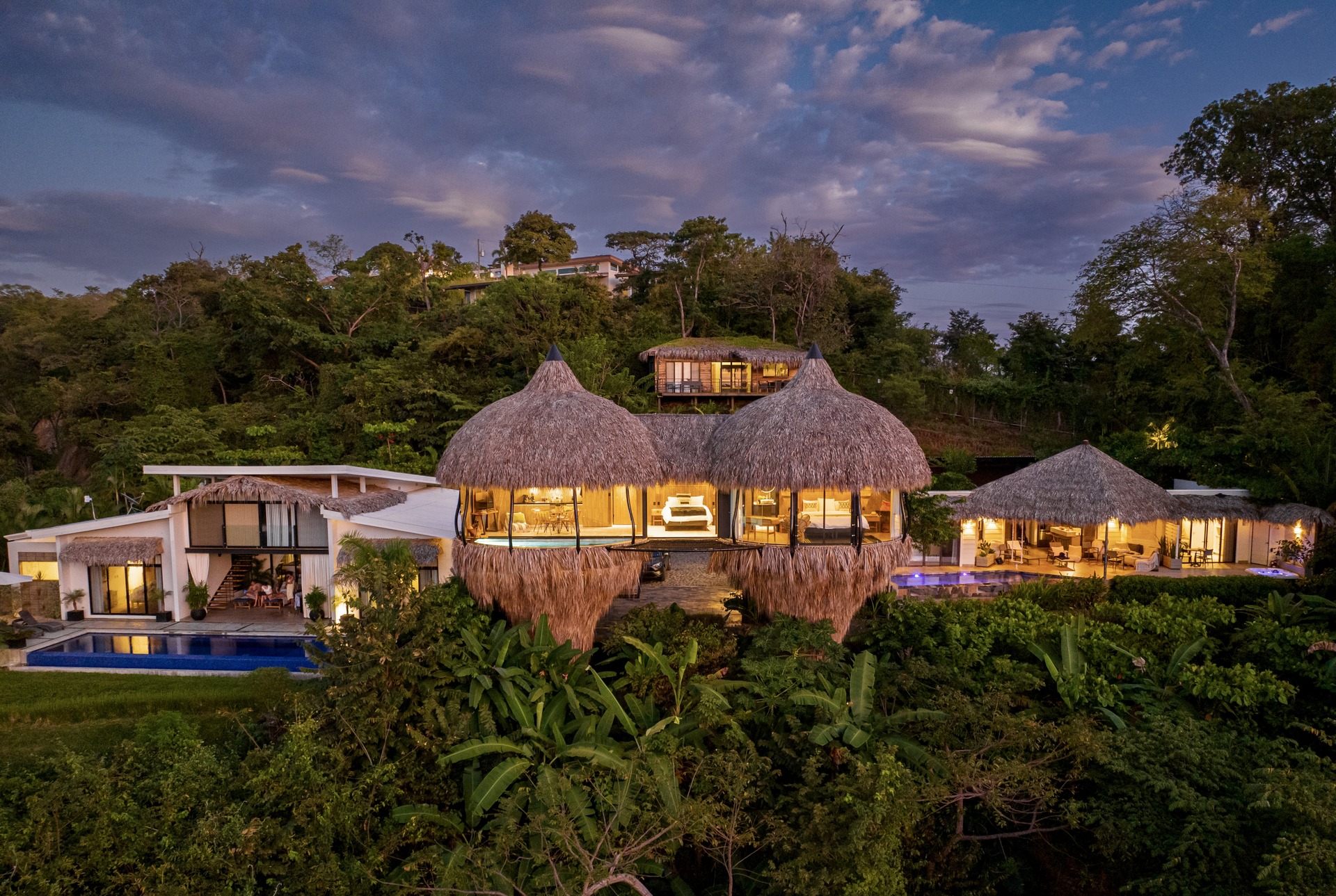 Cocoon Tamarindo rental property with thatched-roof villas, infinity pool, and lush jungle views at sunset | Costa Rica Real Estate CR