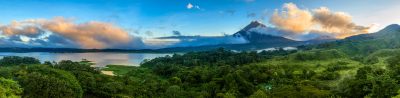Panoramic view of Lake Arenal with lush green hills and Arenal Volcano at sunrise.