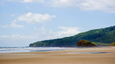 Playa Grande beach in Costa Rica with golden sand, ocean waves, and green hills under a blue sky.