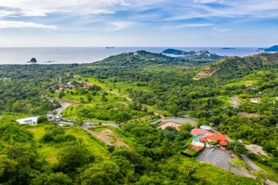 Aerial view of Mar Vista Playa Flamingo Costa Rica with green hills, winding roads, and Pacific Ocean coastline in the distance.