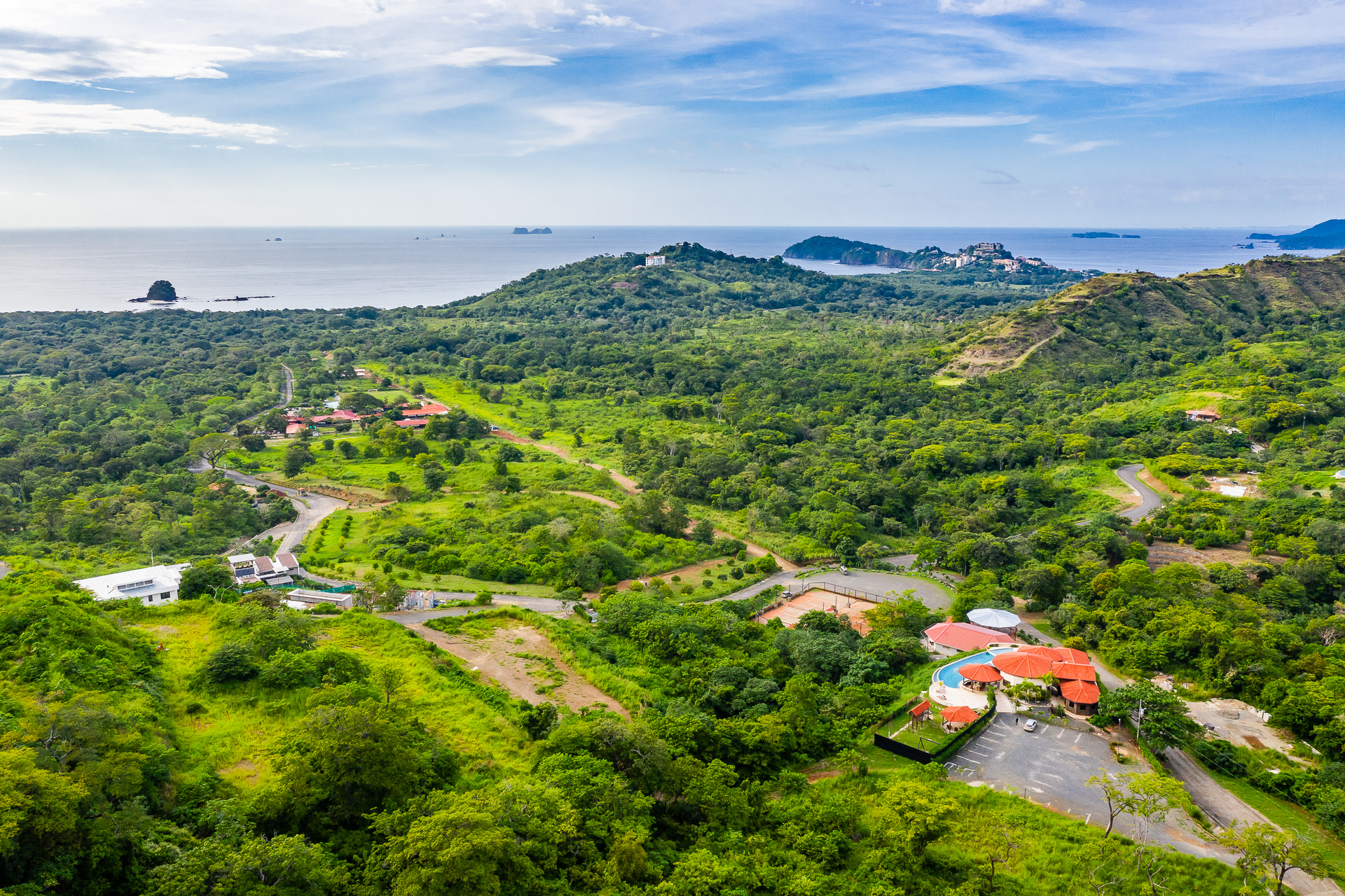 Aerial view of Mar Vista Playa Flamingo Costa Rica showing lush greenery, hillside roads, homes, and Pacific Ocean coastline in the distance.