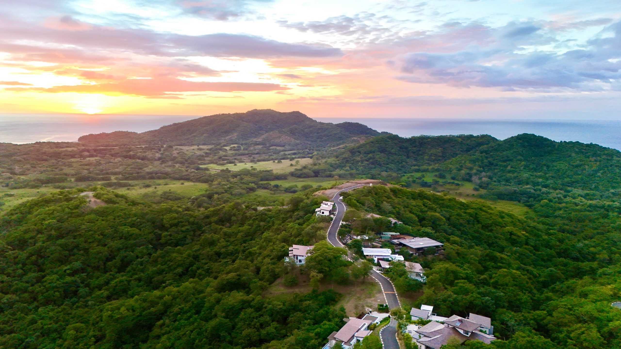 Aerial view of Las Ventanas de Playa Grande Costa Rica with hillside homes, green valleys, and Pacific Ocean at sunset.