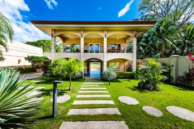 Two-story beachfront home with arched balcony, tropical garden path, and direct ocean access in Playa Potrero