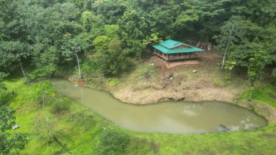 Aerial view of a cabin beside a pond on a Rare 58-Hectare Rainforest Property near La Fortuna, surrounded by dense jungle.