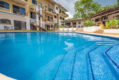 Large resort-style pool with lounge chairs, tropical landscaping, and condo buildings in Tamarindo, Costa Rica at Eleri 17.