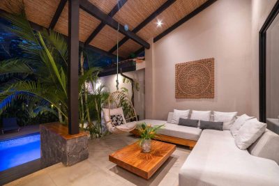 Covered outdoor lounge at Villa Nalú Hacienda Pinilla with seating area, wood ceiling, and tropical plants beside pool