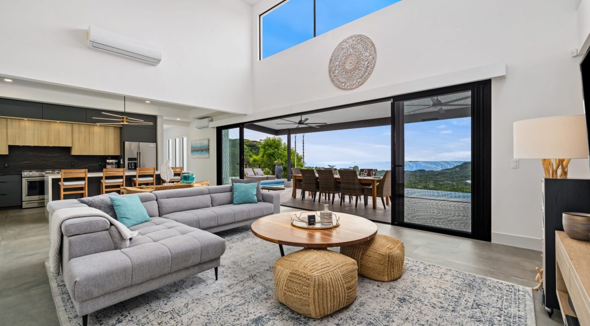 Modern living room with gray sectional sofa, glass doors, and terrace with ocean views