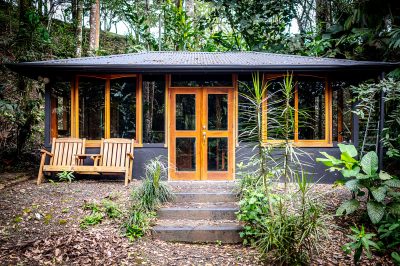 Arenal Lake & Volcano View Tropical jungle cabin with wooden doors and windows surrounded by lush greenery in Tejona, Costa Rica