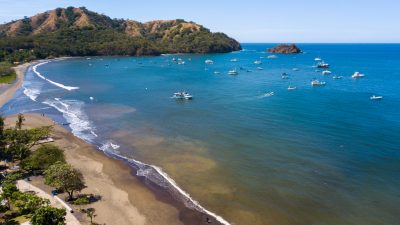 Aerial view of Playas del Coco beach in Costa Rica with anchored boats, calm waters, and coastal real estate area.