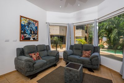 Living room of Portofino A4 condo with two sofas, large windows, garden views, and tropical landscaping.