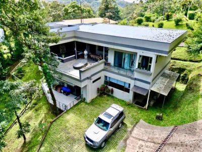 Modern two-story luxury home in Rainbow Bay Lake Arenal surrounded by lush greenery with mountain and garden views.