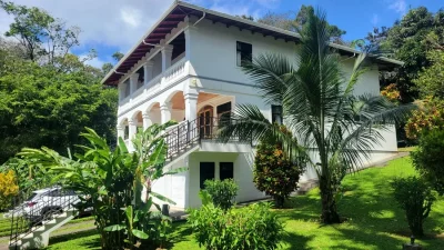 Two-story white home with balconies and arches, surrounded by tropical gardens in Rainbow Bay Estates near Nuevo Arenal.