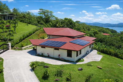 Aerial view of Villa Brisa Guanacaste Costa Rica showing solar panels, red metal roof, driveway, and green hills near Lake Arenal.
