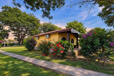Yellow condo with a red-tile roof surrounded by flowering tropical gardens and mature shade trees