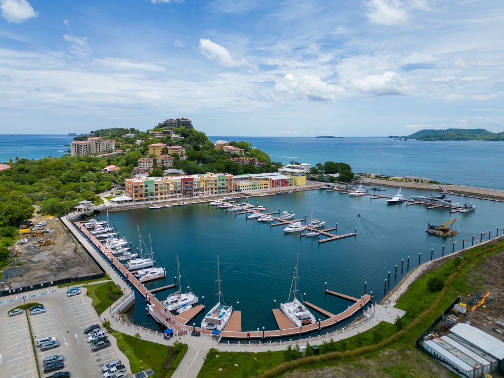 Aerial view of Flamingo Marina with yachts, waterfront buildings, tropical hills, and the Pacific Ocean.