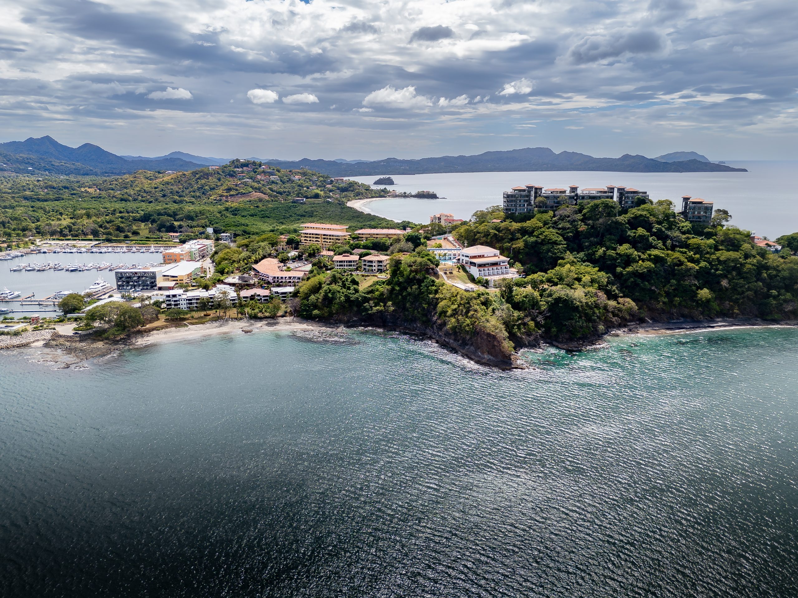 Aerial view of Playa Flamingo Marina, forested hills, coastal buildings, beaches, and the Pacific Ocean in Guanacaste.