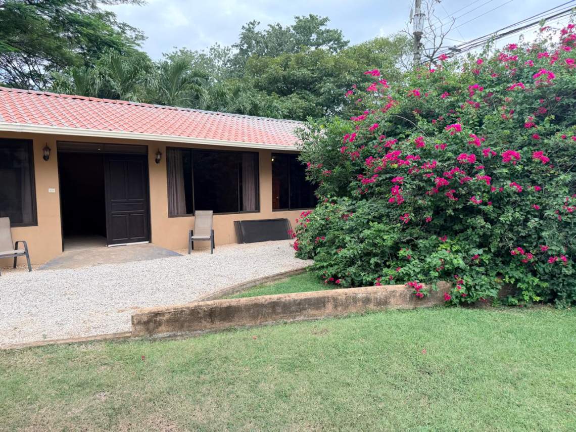 Casa Feliz exterior with lawn, flowering garden, and gravel walkway