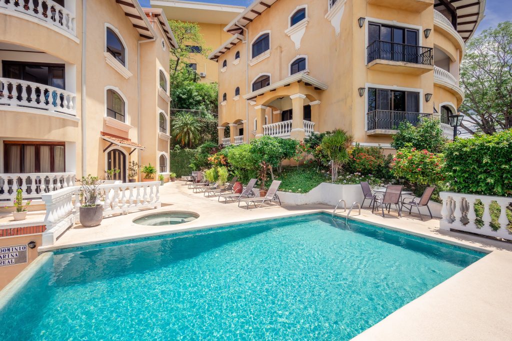 The Flamingo Marina Real community pool is surrounded by landscaped gardens, lounge chairs, and the distinctive architecture of the residential complex.