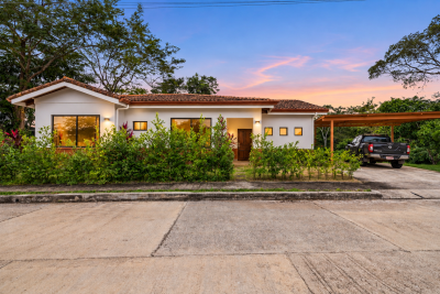 Casa Monos exterior with white walls, red tile roof, tropical landscaping, covered carport, and softly lit evening sky.