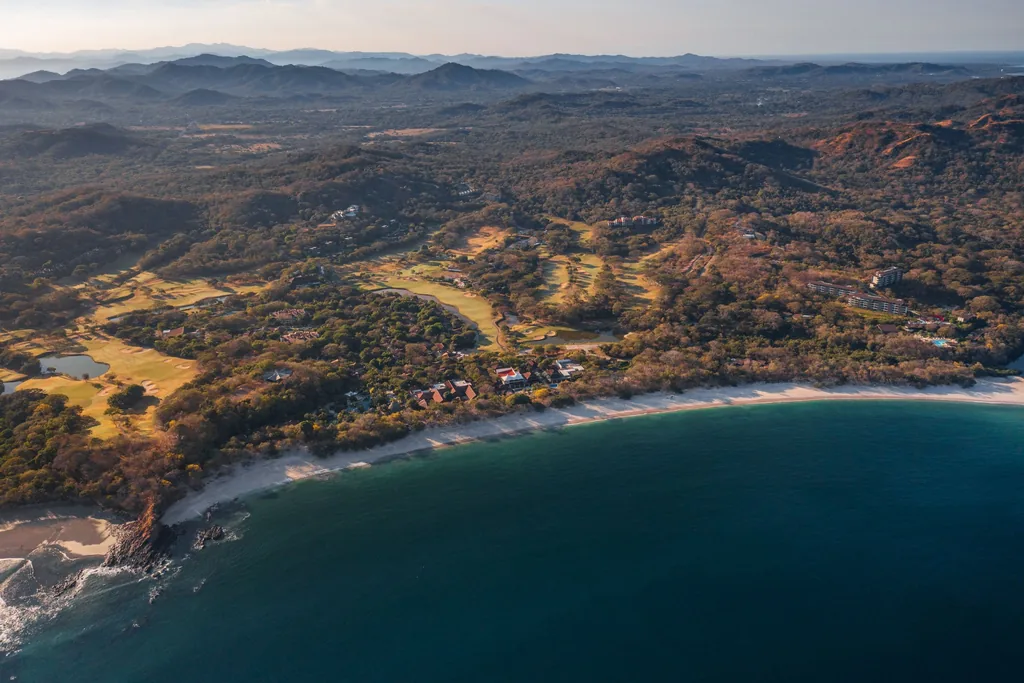 Golden-hour aerial of Reserva Conchal's beach, golf course, and coastline, Guanacaste, Costa Rica