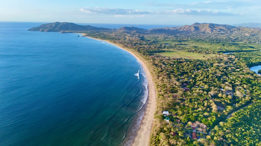 Aerial view of a Guanacaste, Costa Rica beach town with homes and roads extending inland from the coast into the hills