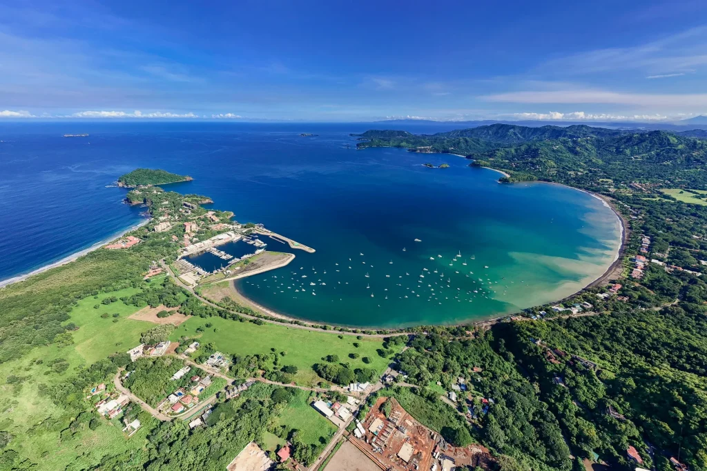 Aerial view of Playa Flamingo's crescent bay and beach near Mar Vista, with sailboats anchored off the marina and the Guanacaste coastline beyond, Costa Rica