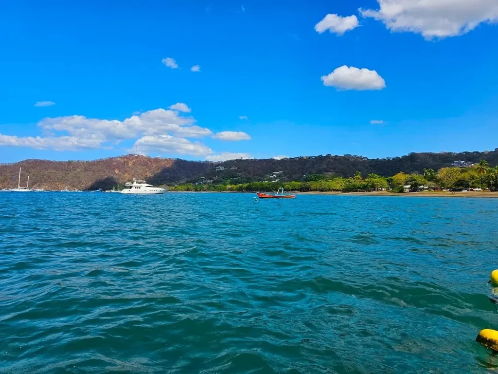 View across Playa Flamingo bay from the water, with a yacht anchored off the tree-lined shore near Mar Vista, Costa Rica