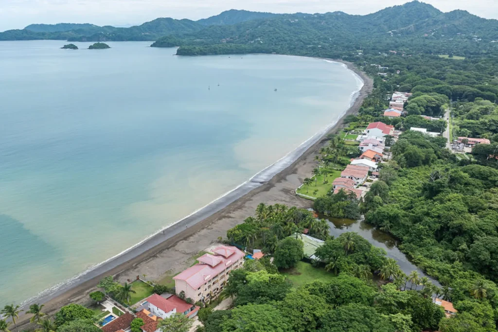 Aerial view of Playa Potrero, Costa Rica, with beachfront homes and condos along the curve of Potrero Bay and forested hills behind