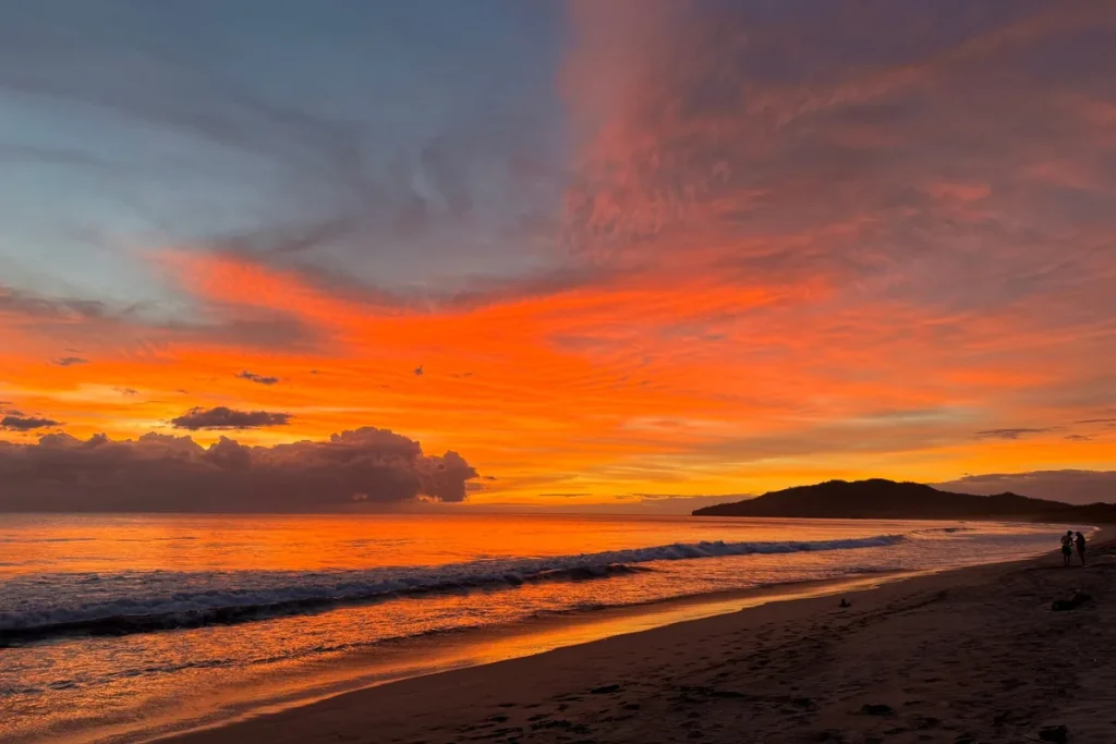 Sunset over the surf at Playa Grande, with the beach curving toward the headland in Guanacaste, Costa Rica
