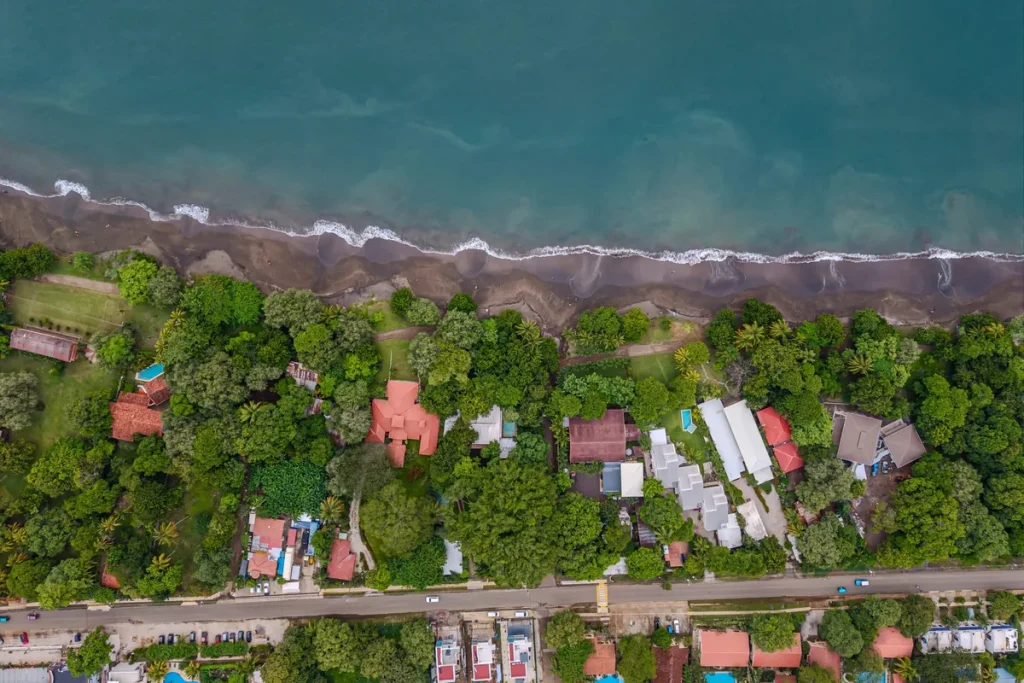 Aerial view of Playas del Coco's grey-sand beach, with tree-lined beachfront homes and the coastal road